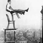 image for A daredevil balances on the back legs of a chair atop other furniture, 20 stories up in New York, circa 1920.