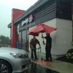 image for A Wendy's employee using an outdoor table umbrella to walk an elderly customer to their car.