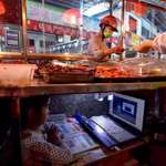 image for Chinese kid taking online class under her parents’ street food stand