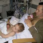 image for A big brother helping his father to give skin to skin contact to his premature twin siblings