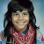 image for My mother in 4th grade in the 70s. Her mother wouldn't let her bring the outfit for picture day so she brought it with her and changed at school. A patchwork cowboy shirt, a bandana and a velvet Pakistani vest.