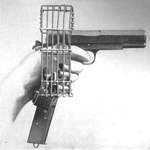 image for US .45 cal M1911 pistol with extended magazine and brass catching cage. In the early days of WW1 and aircraft didn't have machine guns, enemy pilots would shoot at each other with pistols. The cage prevented the spent shells from ejecting onto the cockpit floor and interfere with the foot controls