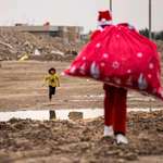 image for A child runs towards a man dressed as Santa Claus as he walks with a sack of gifts in a slum in Iraq