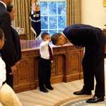 image for Obama bending over so that the son of a White House staff member can pat his head. (2009)