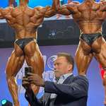image for Arnold Schwarzenegger taking a selfie while men flex their butts behind him