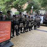 image for Riot cops line up next to a sign at Texas University.