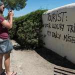 image for A tourist takes a picture of graffiti reading ‘Tourist: your luxury trip – my daily misery’