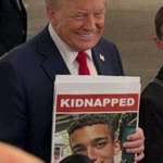 image for Trump smiling while holding an Oct. 7 'kidnapped' poster during a remembrance event in Queens