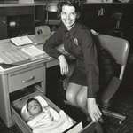 image for A policewoman tends a baby girl who was found alone at a hotel room in Los Angeles, 1971