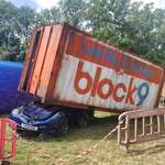 image for OC. Tesla with a Fascism numberplate squashed by a shipping container at Glastonbury Festival, UK.