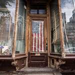 image for A dilapidated storefront with an American flag draped over the front door.