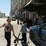 image for ​Two girls in Gaza in Eid clothes carrying a broken chair from the rubble to use as cooking fuel
