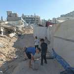 image for A barefoot boy holding his new shoes as he carries a water container in Gaza today amidst the rubble